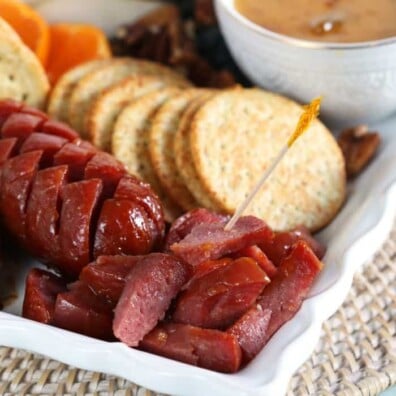 baked salami cut up on a plate with toothpick and crackers