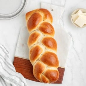 Golden brown challah bread on a marble cutting board with butter on the side.