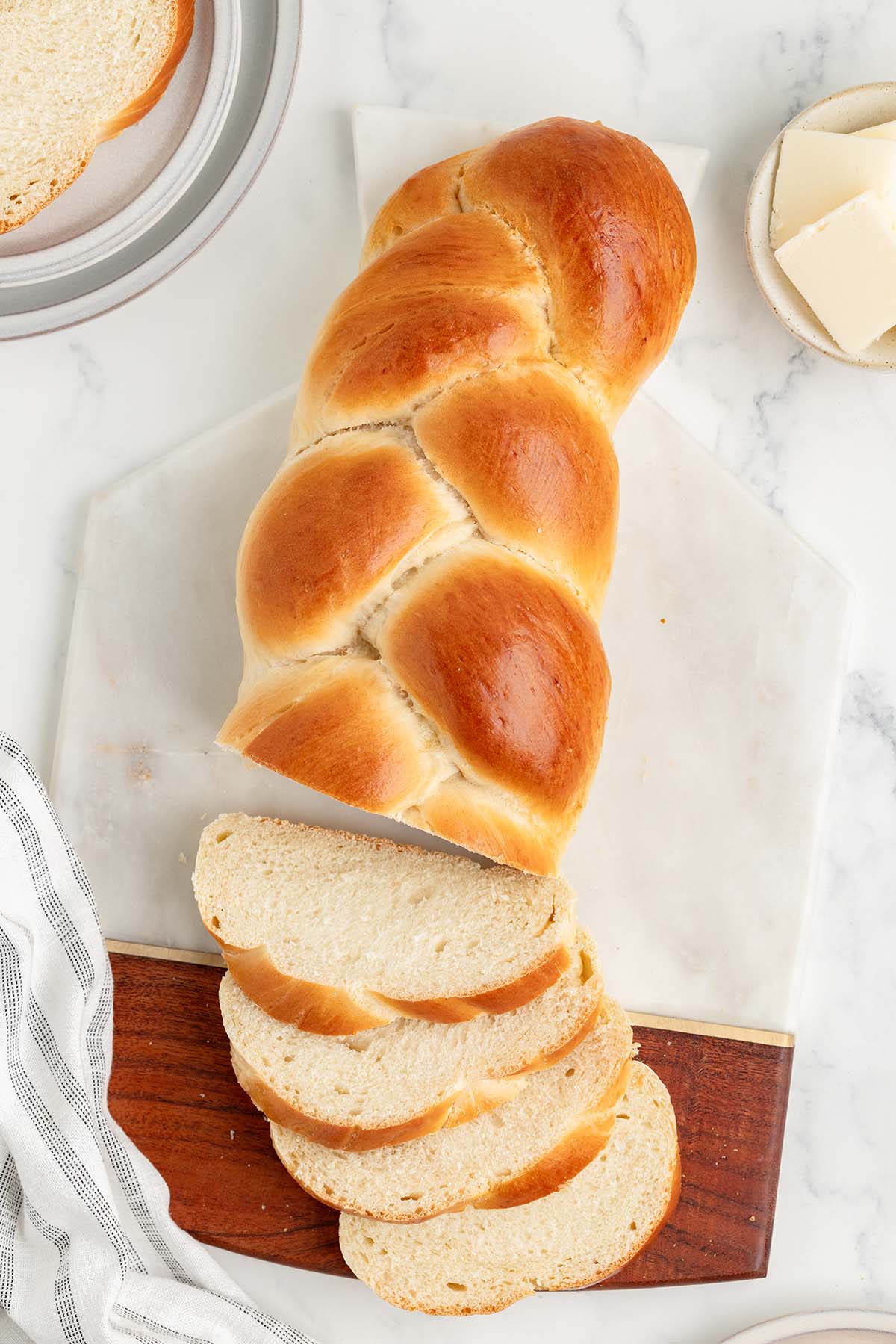 Sliced challah bread on a marble and wood cutting board with butter on the side.