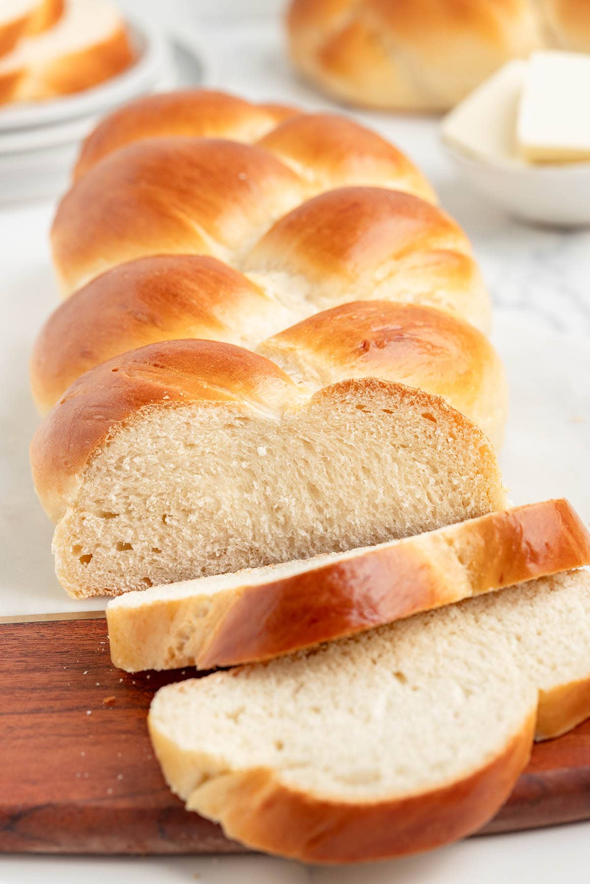 Sliced challah bread on a wooden board with butter in the background.