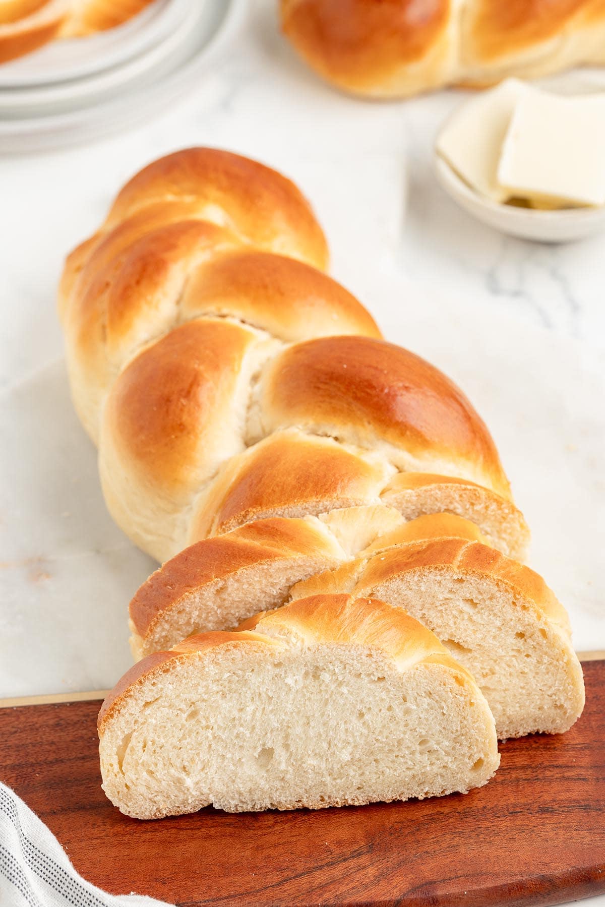 Sliced challah bread on a wooden board with butter in the background.