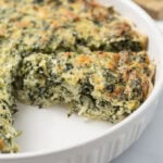 Spinach pie in a white baking dish with a slice removed.