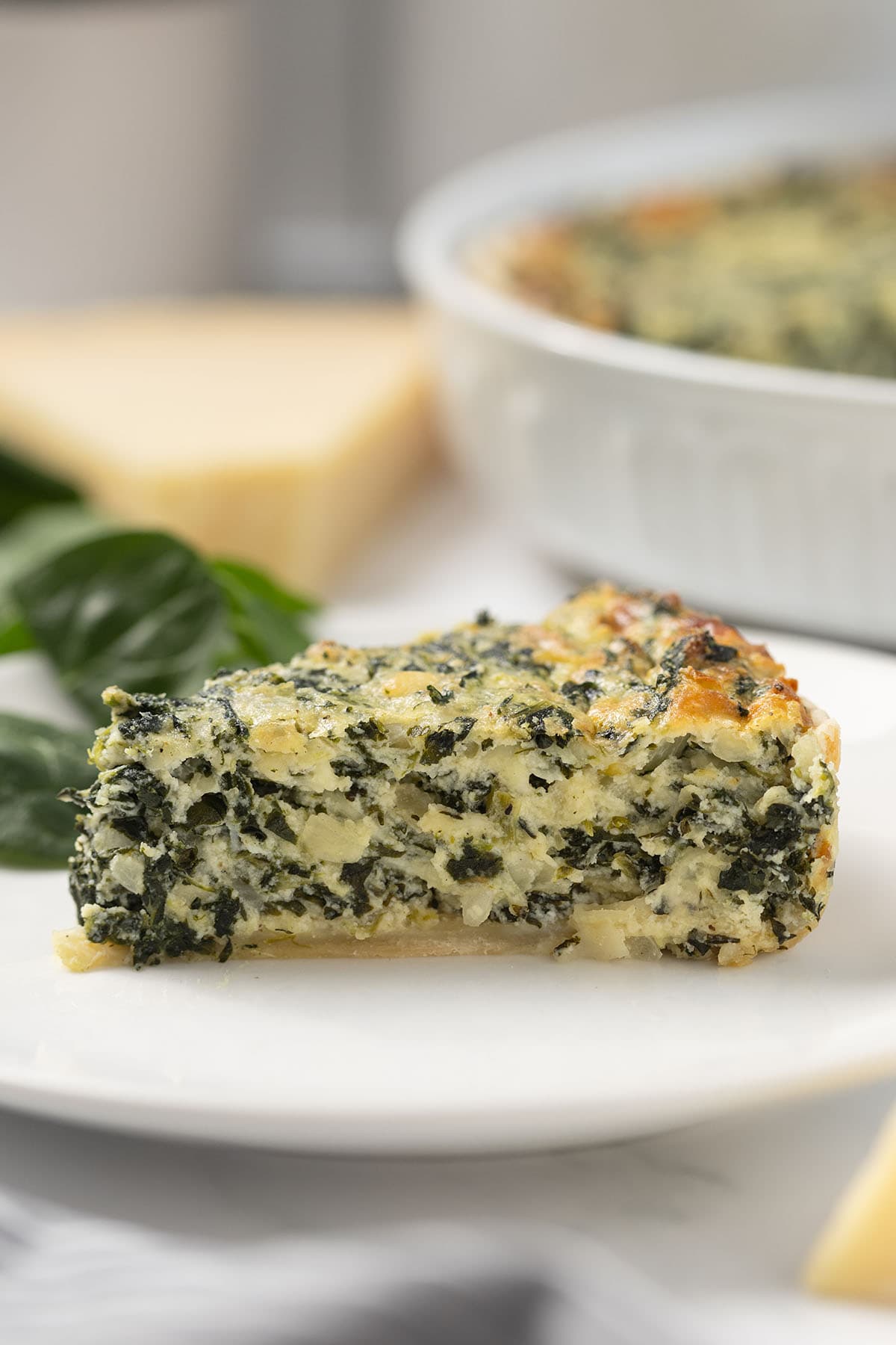 Slice of spinach pie on a white plate, showing a cheesy spinach filling with a flaky crust.