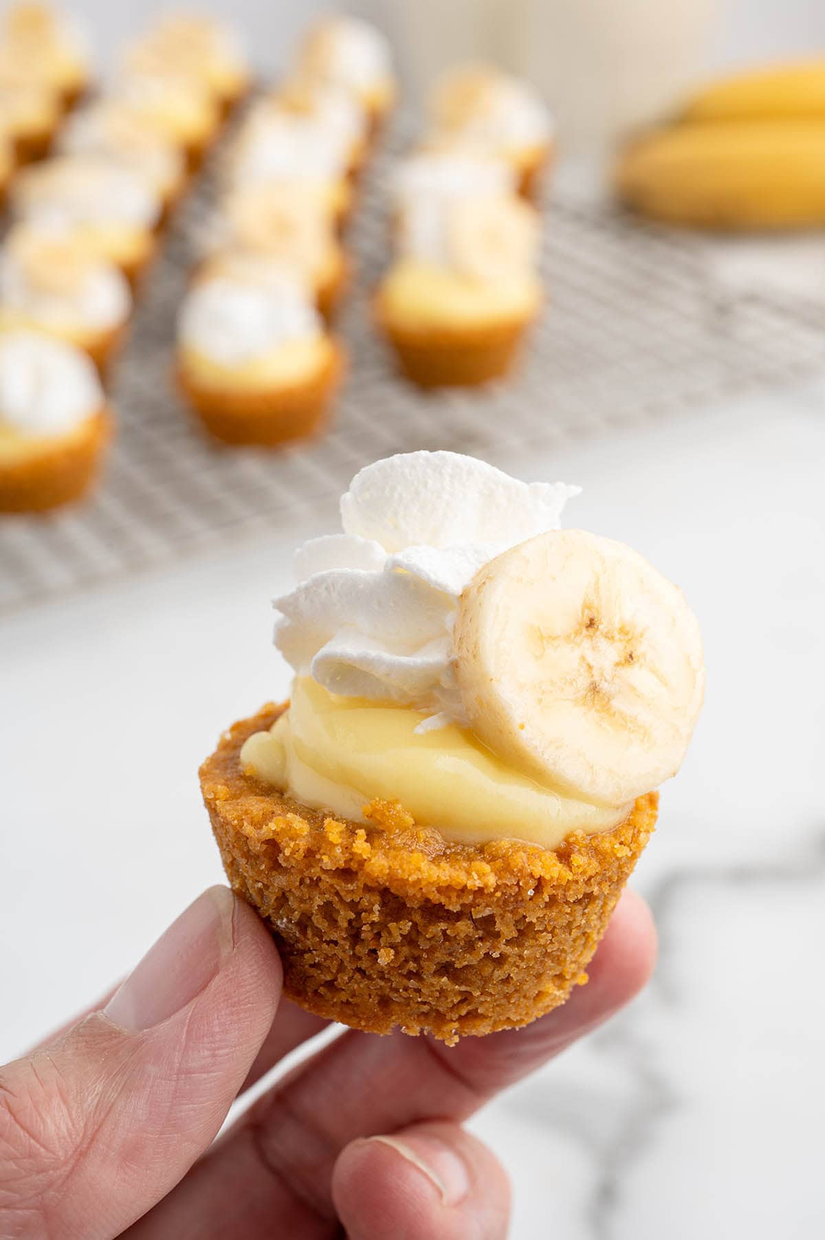 Hand holds mini banana cream pie with whipped cream and banana slice on top.