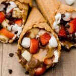 A waffle cone stuffed with marshmallows strawberries bananas chocolate and caramel
