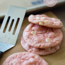 White chocolate strawberry cookies on a wood board with a spatula