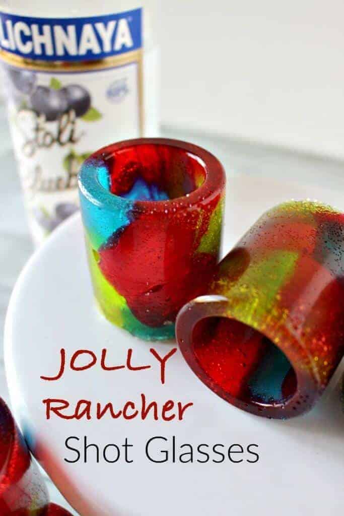 two Jolly Rancher shot glasses on a white plate with vodka in the background