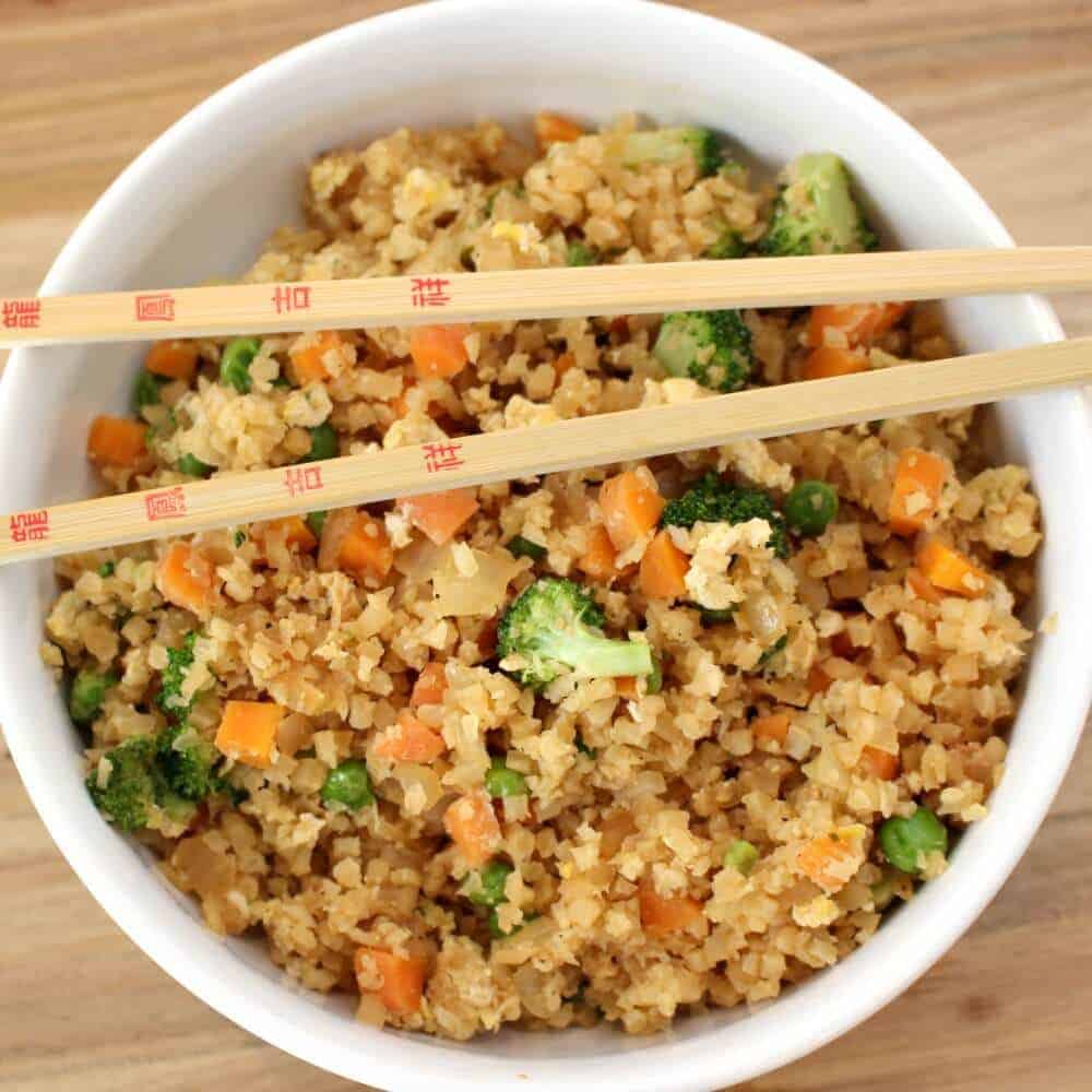Cauliflower fried rice with carrots and broccoli in a white bowl with chopsticks