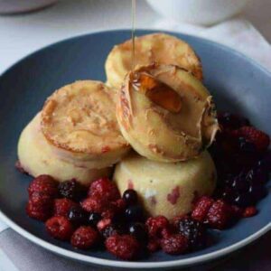 Pancake poppers with berries surrounding it on the black dish