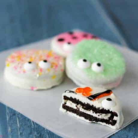 Oreo cookies dipped in chocolate with sprinkles and eyes on them to look like monsters or critters on a white plate