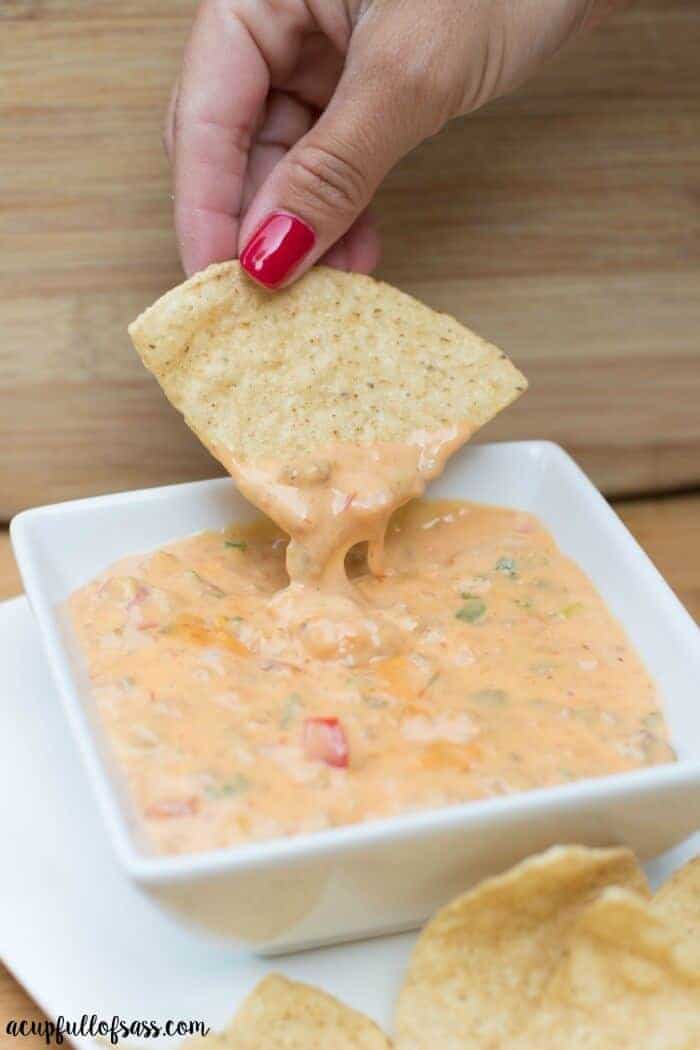 Crockpot nacho dip in a white dish with a chip being dipped into it