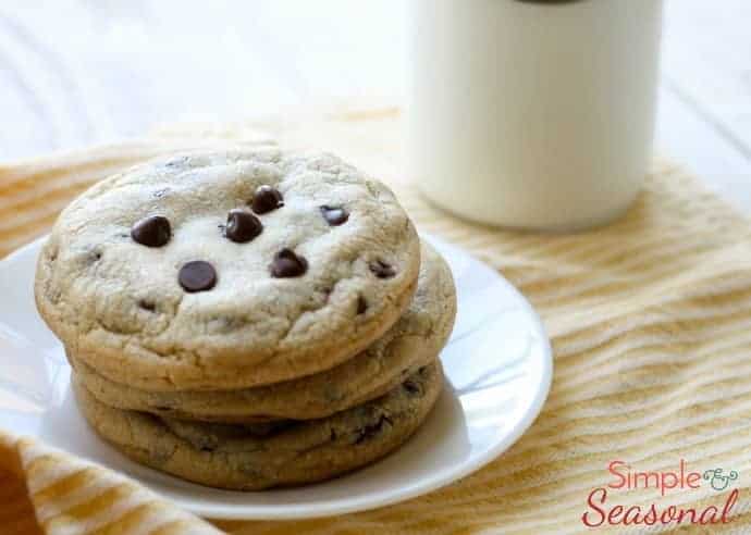 Chocolate chip cookies stacked on a white plate with a cup of coffee in the background
