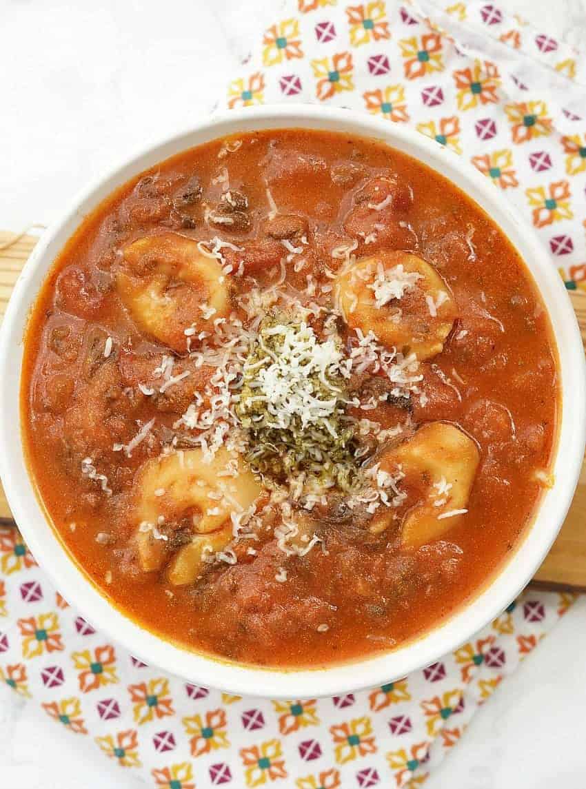 A close up of a bowl of soup, with Tomato and Tortellini