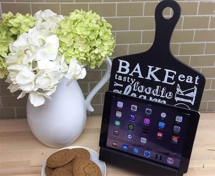 A tablet holder next to a picture full of flowers and a plate of cookies