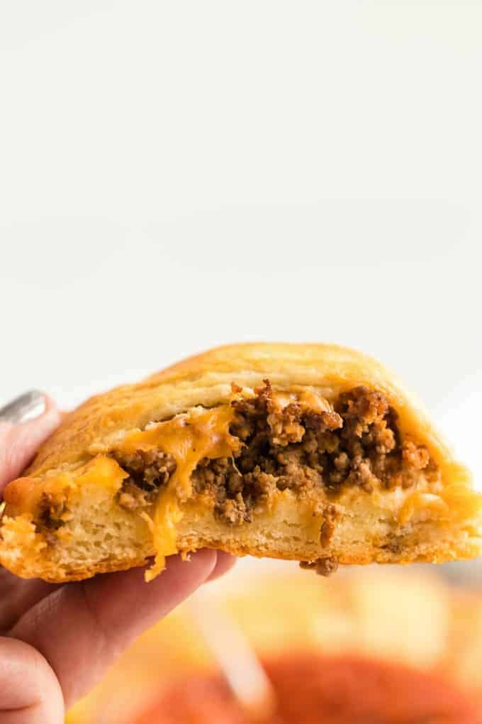 Piece of beef taco ring being held with cheese and beef coming out