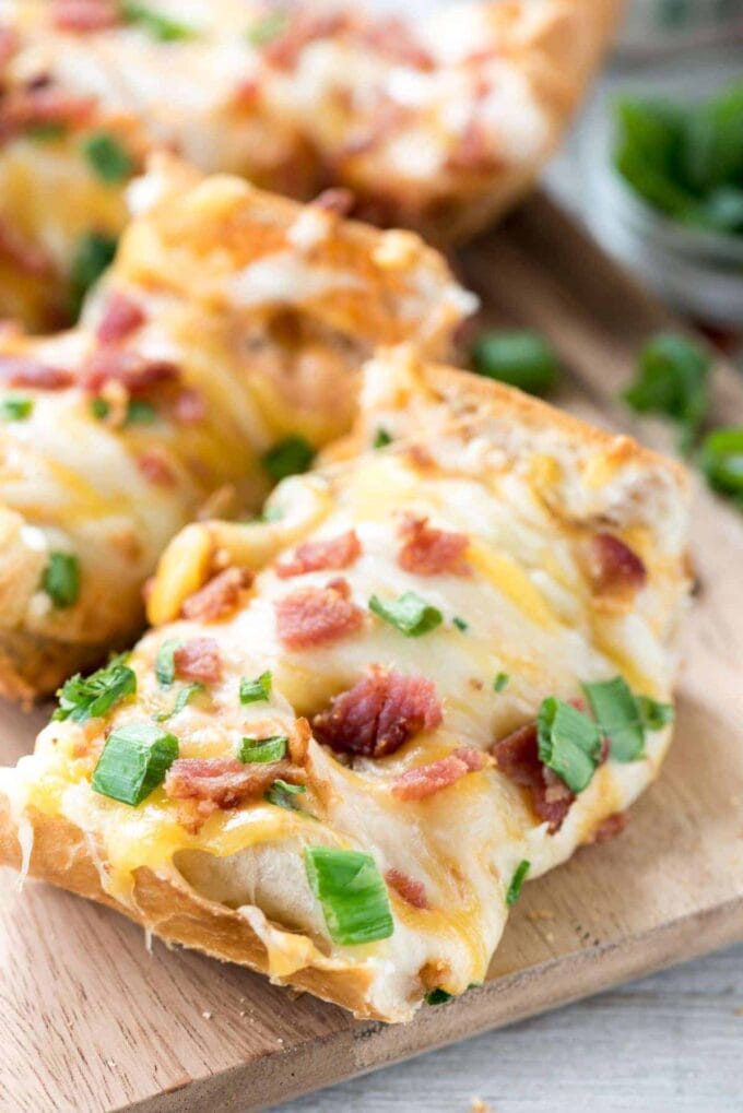 A close-up of cheesy bacon ranch French bread pizza on a cutting board