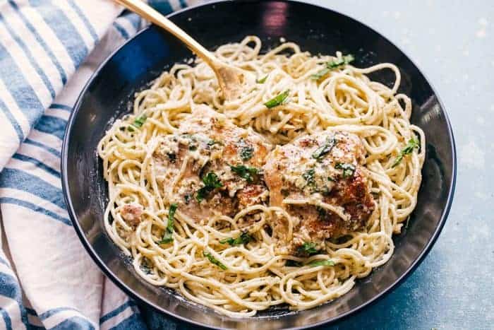 Bowl of creamy pesto chicken thighs served over spaghetti, garnished with basil and parmesan.