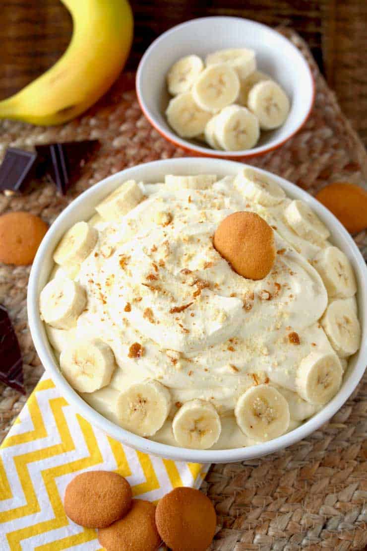 Banana cream pie dip in a white bowl with yellow lemons and bananas on top