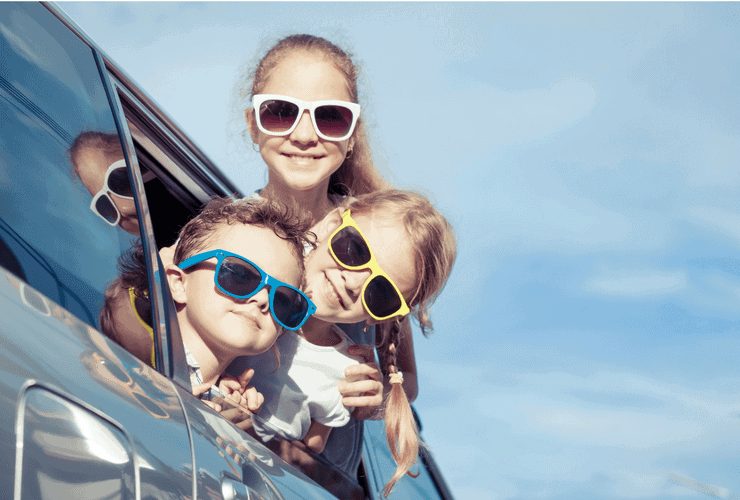 Three kids wearing sunglasses with their head out the car window