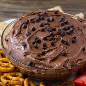 A bowl of brownie batter dip with pretzels around it and chocolate chips on top