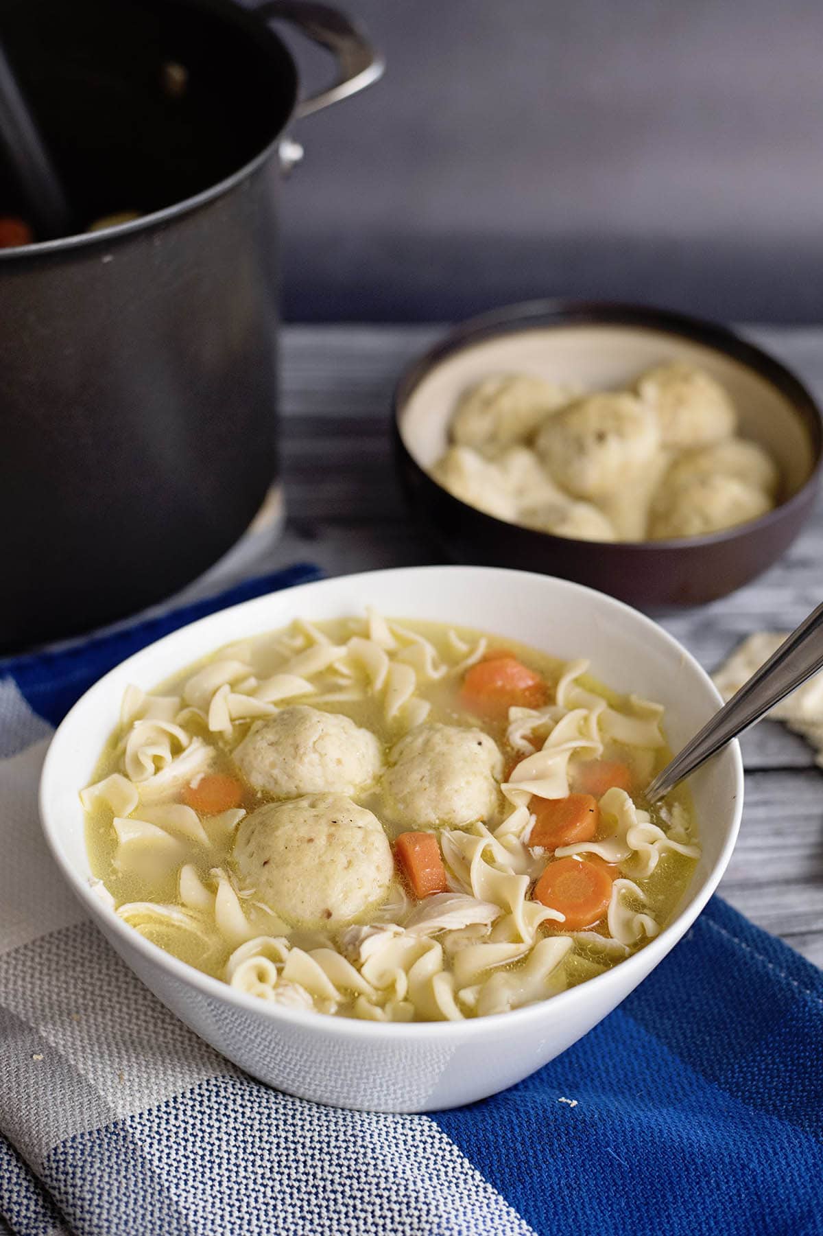 Soup Recipe with matzo balls, egg noodles, carrots, and broth served in a white bowl