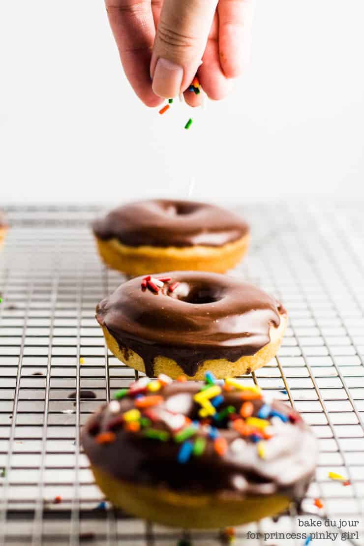 A set of 3 chocolate frosted doughnuts. Sprinkling some sprinkles over the middle doughnut