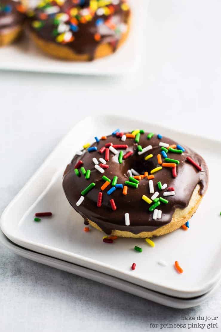 A Chocolate Frosted Doughnut on a white plate with another doughnut in the background