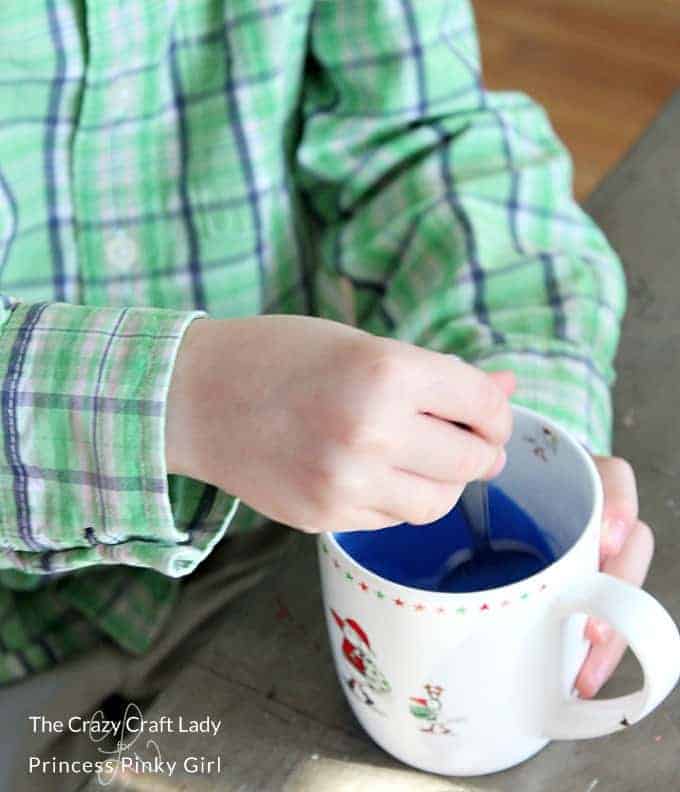 A child\'s hand stirring a mug of blue paint