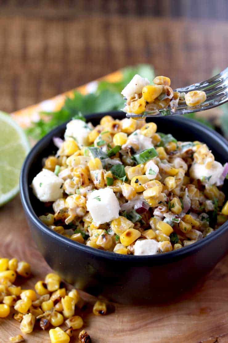 A bowl of food with a fork with corn on it and cojita cheese