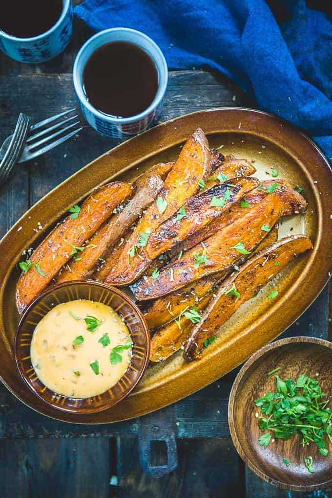 Baked sweet potato wedges on a platter with a dip