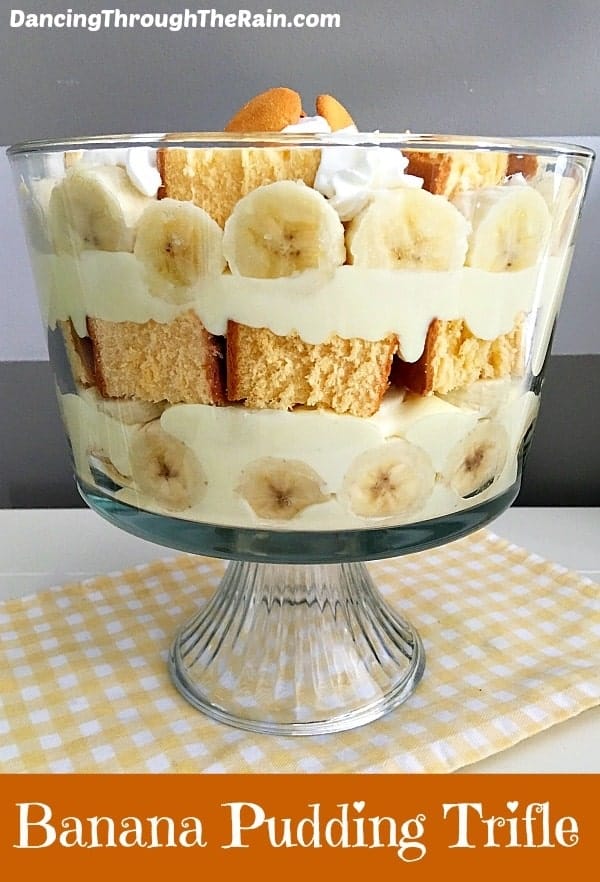 A banana pudding trifle in a glass bowl with a checkered yellow dish towel underneath it