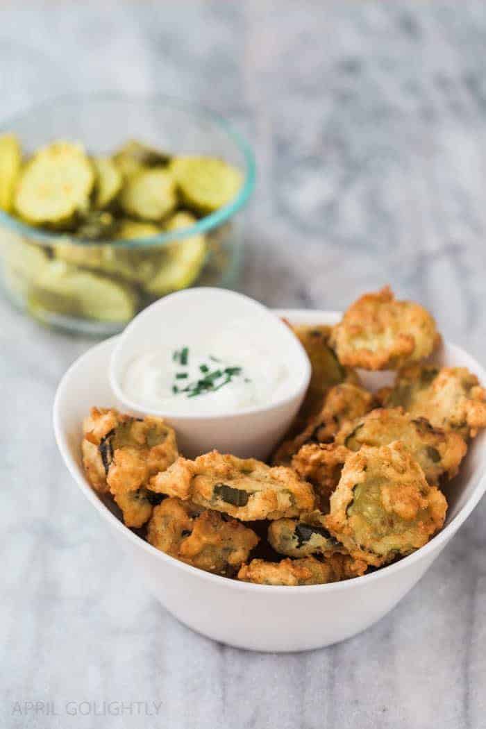 Deep fried pickles with a dipping sauce in a white bowl