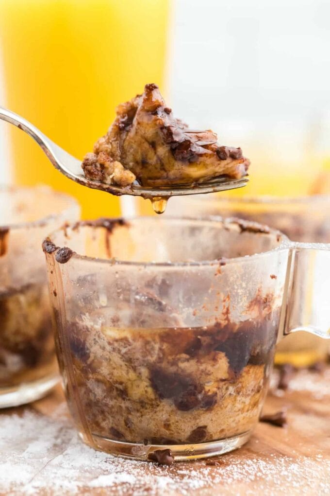 A mug with French toast in it with a spoon full dripping with syrup