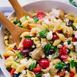 A bowl of Greek chicken pasta salad with wooden serving spoons