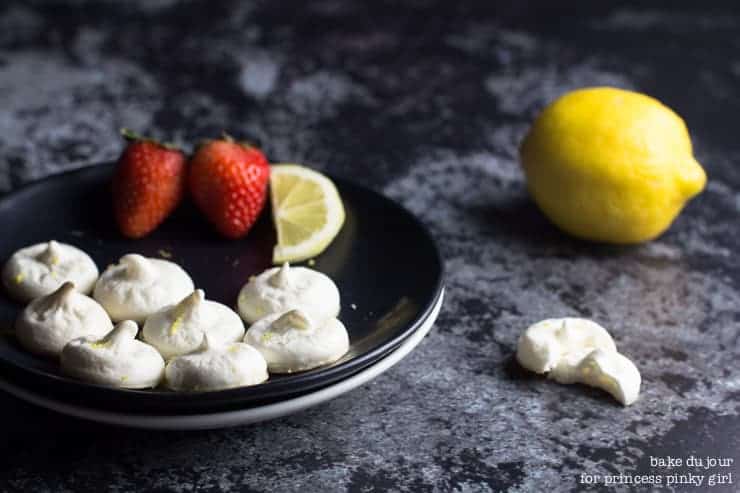 Lemon meringue cookies and a black plate with strawberries and a lemon wedge and a full lemon in the background