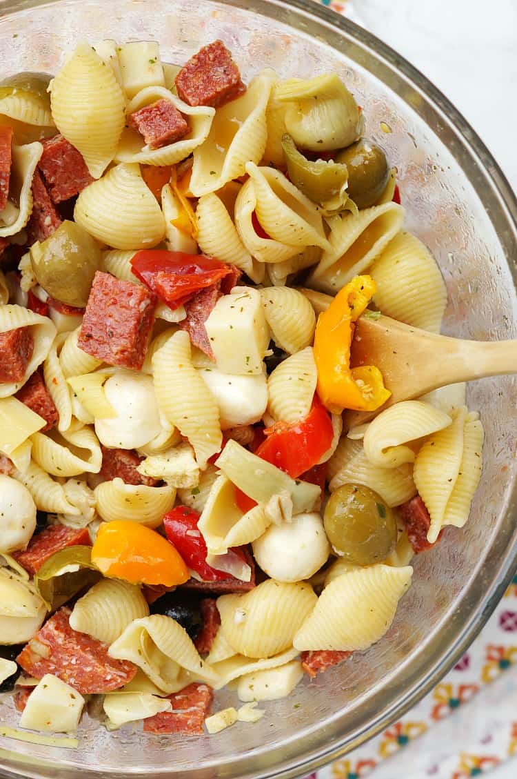 A glass bowl filled with pasta salami peppers olives and cheese