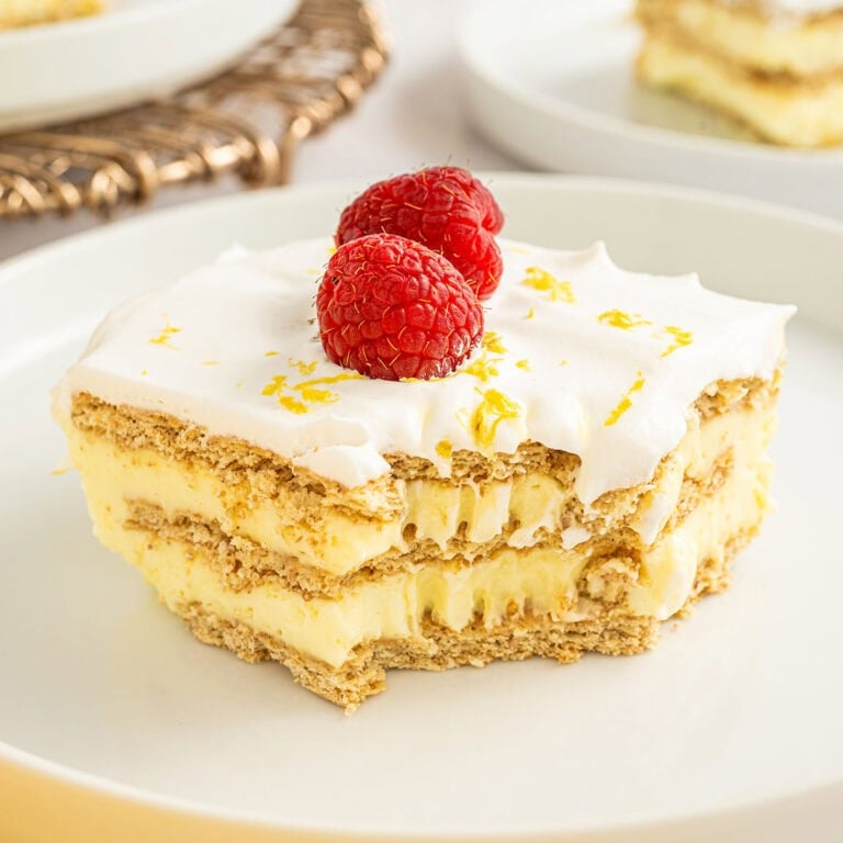 Slice of lemon icebox cake with graham cracker layers, creamy lemon filling, whipped topping, and two fresh raspberries on top.