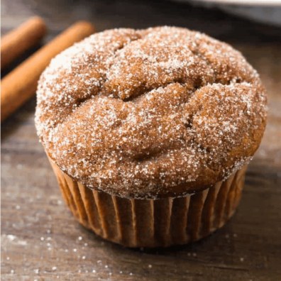 A pumpkin spice muffins with sugar on top and cinnamon sticks behind it