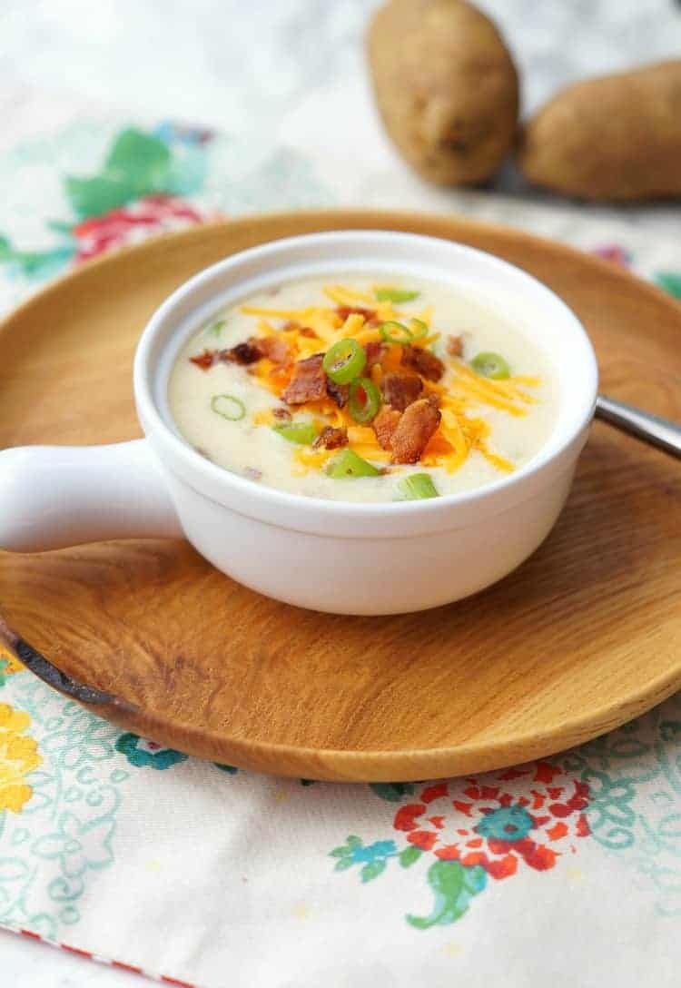 A bowl of loaded potato soup on a wooden plate