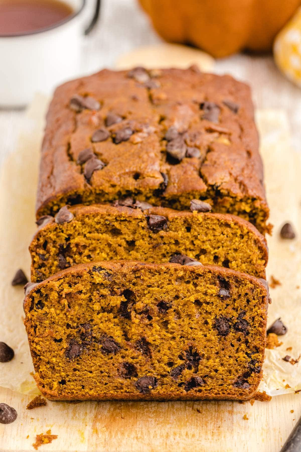 a loaf of chocolate chip pumpkin bread sliced on top of wooden board. 