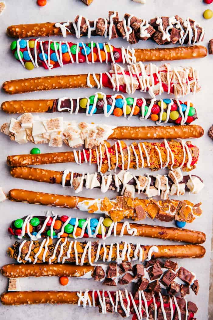 chocolate covered pretzel rods on a sheet pan coated in different crushed candy. 