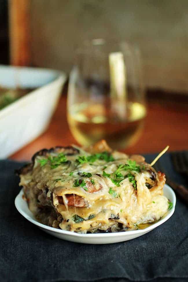 Mushroom and spinach lasagna and a white plate with a glass of wine behind it