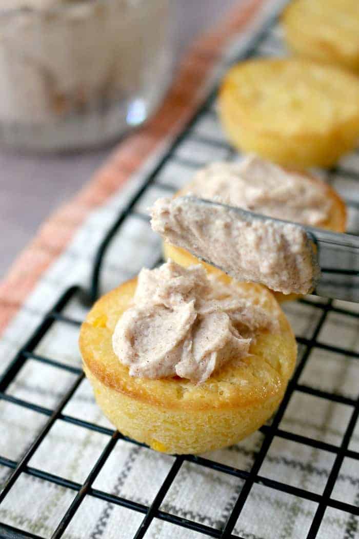 Mini cornbread muffins with cinnamon butter spreading on top with a knife