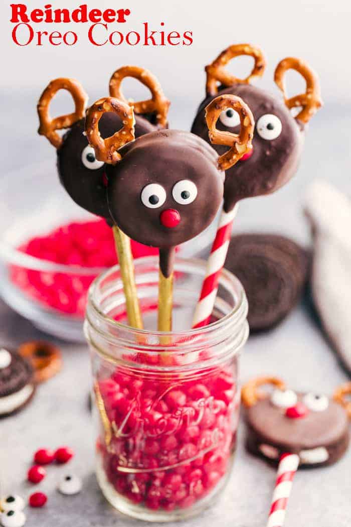 three reindeer oreo cookies standing in a jar filled with red hot candy.