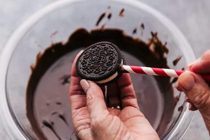 An Oreo cookie with a straw being inserted into it over a bowl of melted chocolate