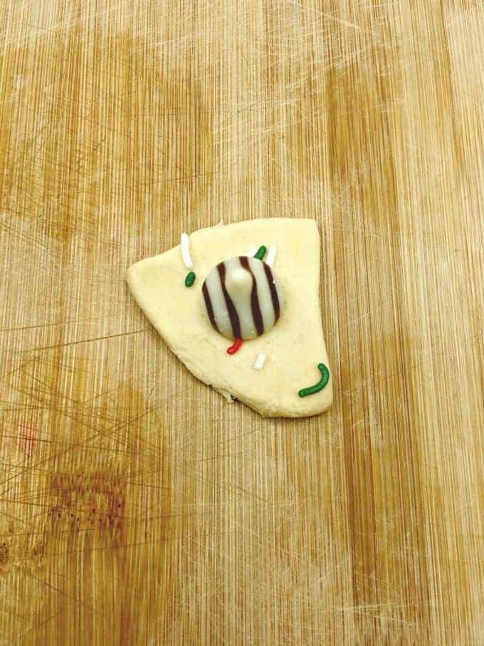 A piece of crescent roll with a Hershey hug and Christmas colored sprinkles on it