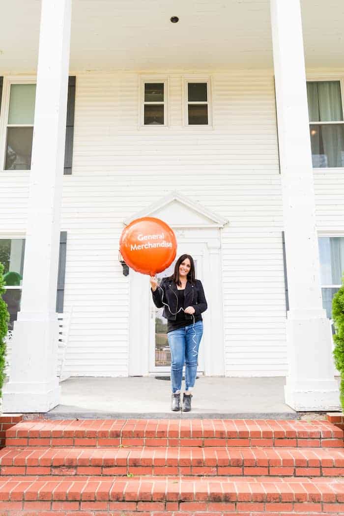 Woman holding orange balloon with the words general merchandise