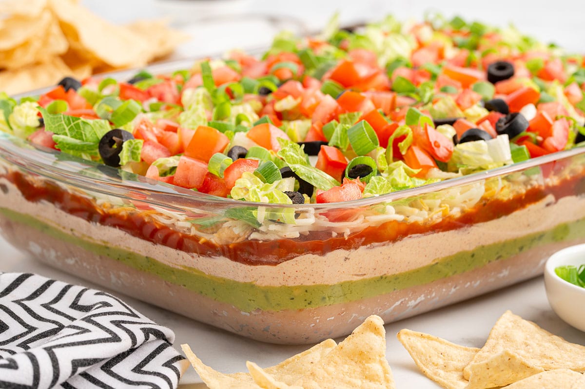 7 Layer Dip in a baking dish topped with lettuce, tomatoes, olives, and green onions.