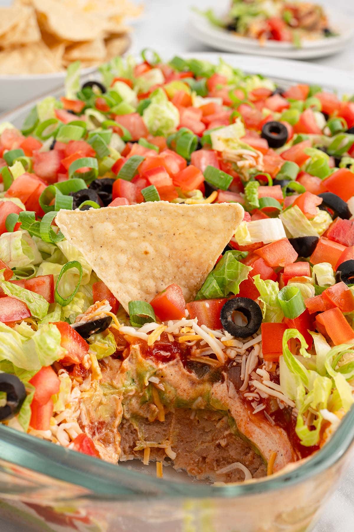 7 Layer Dip in a baking dish with a tortilla chip partially dipped into it.