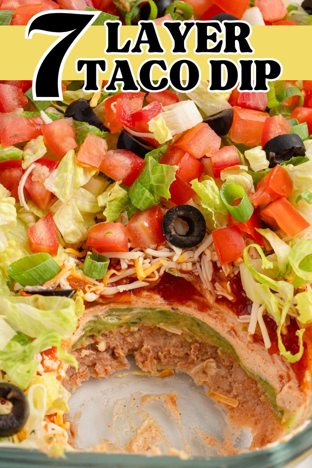 7 layer taco dip served in a glass baking dish with some part of it that has been scooped out